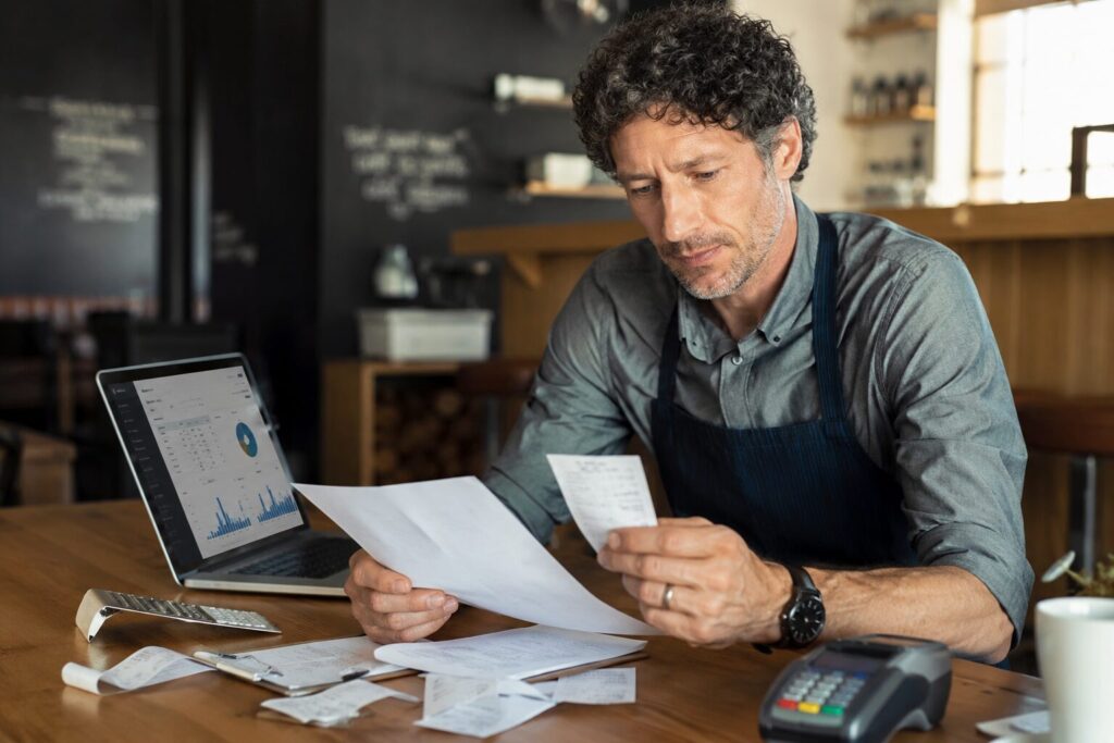 Business owner reviewing receipts, merchant statements, and payment reports to identify hidden credit card processing costs and fees.