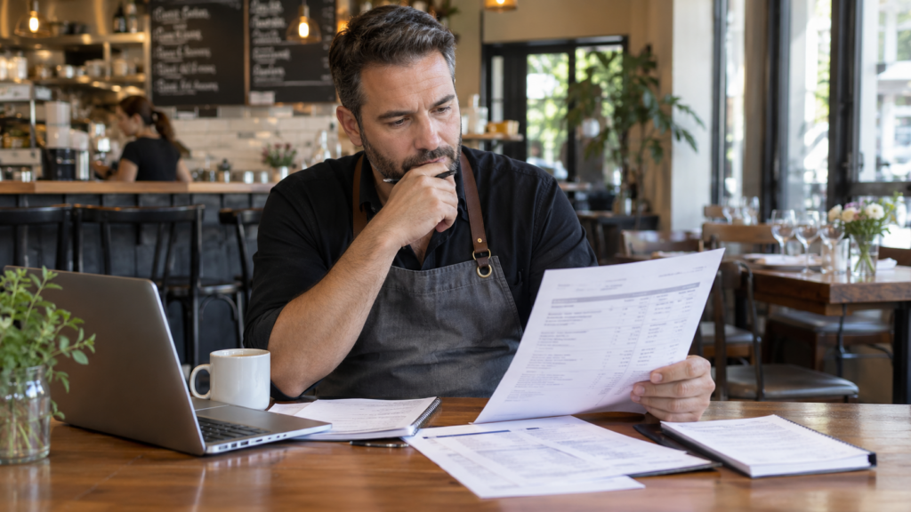 Restaurant owner reviewing a merchant statement and business paperwork inside a restaurant.